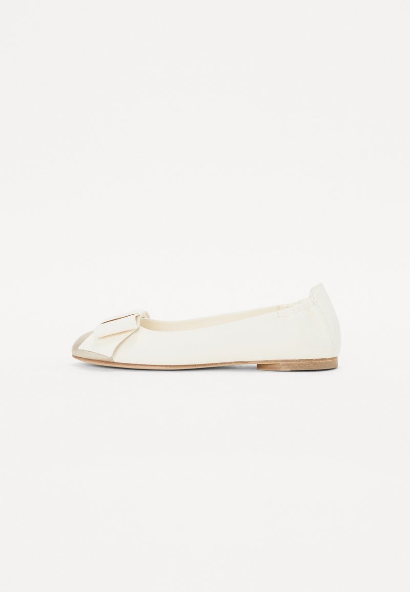 Chaussure plate blanche en matériau lisse, présentant un grand nœud sur le bout, une silhouette ronde et un petit talon en bois.