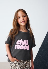 Graues Baumwoll-T-Shirt mit hochgekrempelten Ärmeln und großem pinkfarbenem Schriftzug "chill mood." Kombiniert mit Leopardenmuster-Hose und betont so einen lässigen Look.