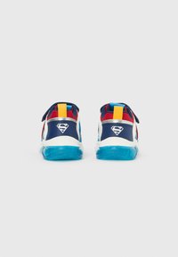 Pari värikkäitä lasten tennareita, joissa on siniset pohjat, punainen ja sininen kangas, keltaiset vetoketjut ja valkoiset Teräsmies-logot koroissa.