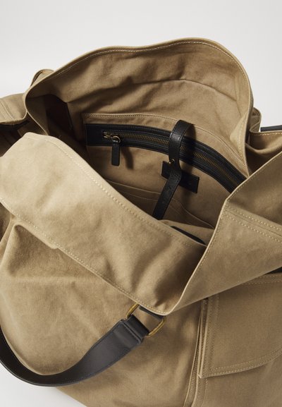 Beige kangaskassi, jossa on rakenteellinen muoto, musta nahkakahva ja sisätaskuja, mukaan lukien vetoketjullinen osio.