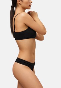 Bralette de algodón negro con tirantes ajustables y bordes festoneados, combinado con bragas negras a la cadera a juego. Textura suave, diseño minimalista.