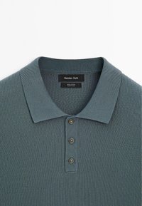 Bawełniana koszulka polo w ciemnym morskim odcieniu. Charakteryzuje się prążkowaną fakturą, kołnierzykiem oraz trzema ciemnymi guzikami przy szyi. Metka z napisem „Massimo Dutti”.