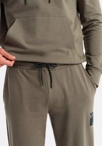 Sudadera y pantalones jogger verde olivo de algodón suave, con un bolsillo canguro, cordón ajustable y un parche de logo prominente.
