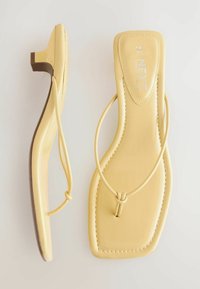 Sandali piatti gialli con una finitura in pelle liscia, cinturini sottili e un piccolo tacco a blocco. Presentano una punta arrotondata e accenti di design minimalisti.