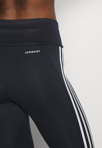Svarta leggings med AEROREADY-logotyp, med en bred midja och vita sidostrecken för detaljer och kontrast. Slät, elastisk tyg.