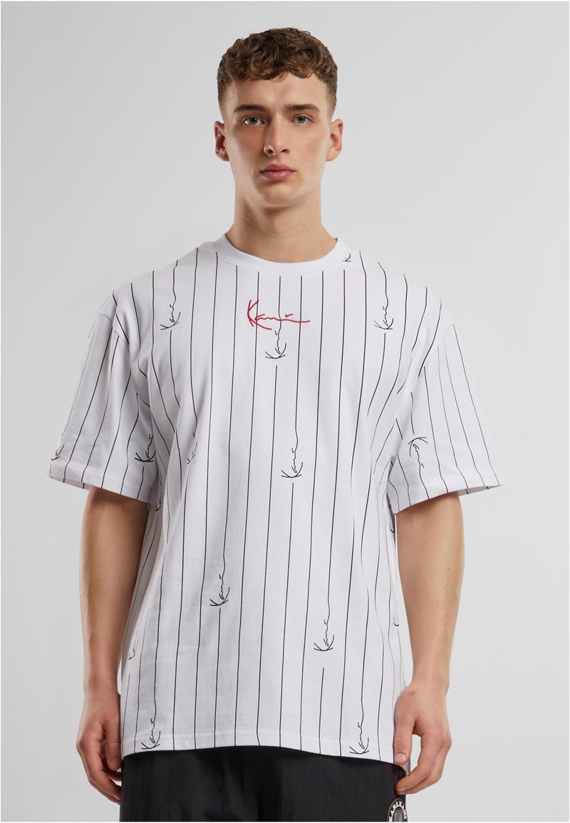 Bílý bavlněný tričko s černými vertikálními pruhy a abstraktními červenými a černými grafikami. Krátké rukávy a volný střih.