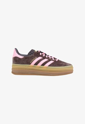 Zapatilla Adidas Gazelle de ante marrón con rayas rosas, cordones rosas y suela gruesa de goma en capas, mostrada de lado sobre fondo blanco.