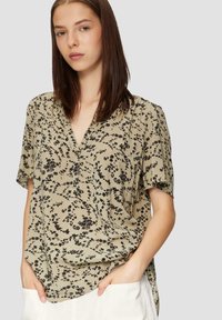 Beige Bluse mit floralem Druck und schwarzen Mustern, kurze Ärmel und V-Ausschnitt. Stilvolles Drapieren und lockere Passform für Komfort.
