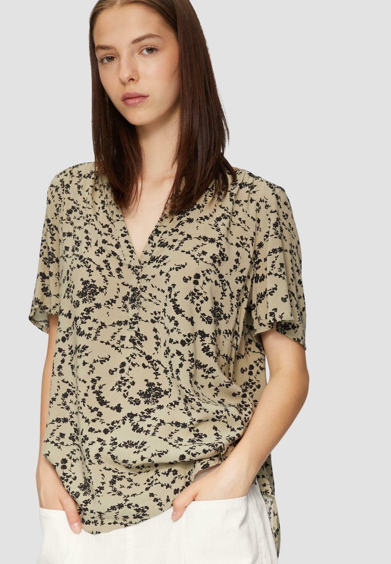 Beige Bluse mit floralem Druck und schwarzen Mustern, kurze Ärmel und V-Ausschnitt. Stilvolles Drapieren und lockere Passform für Komfort.