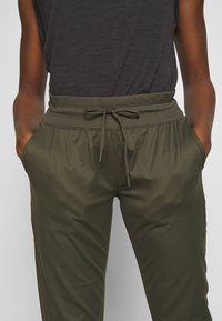 Pantalones jogger en color verde oliva con cintura elástica, cierre de cordón y bolsillos laterales. Están hechos de un material suave y ligero.