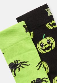 Zelene in črne nogavice z vzorci pajkov in buč. Mehka pletenina, svetle barve in elastični robovi za varen oprijem.