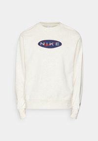 Vitrandig sweatshirt i mjukt tyg med en oval marinblå logga med röda detaljer som säger "NIKE." Klassisk rund halsringning och åtsittande muddar.
