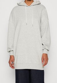Sudadera con capucha de color gris claro, de mangas largas, con cierre de cordón y un bolsillo frontal. Textura suave y corte holgado, diseñada para la comodidad.