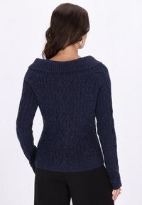 Navyblauer strukturierten Pullover mit breitem Rippkragen, Kabelstrickmuster, langen Ärmeln und figurbetontem Schnitt.