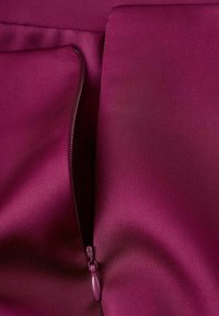 Tissu bordeaux avec une texture lisse, doté d'une fermeture éclair dissimulée sur le côté. Les coutures sont soignées et le matériau semble léger.