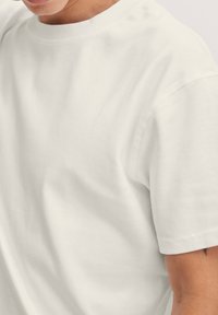 Hvid bomulds-T-shirt med rund halsudskæring og korte ærmer. Stoffet virker blødt og glat med minimalt synlige sømme.