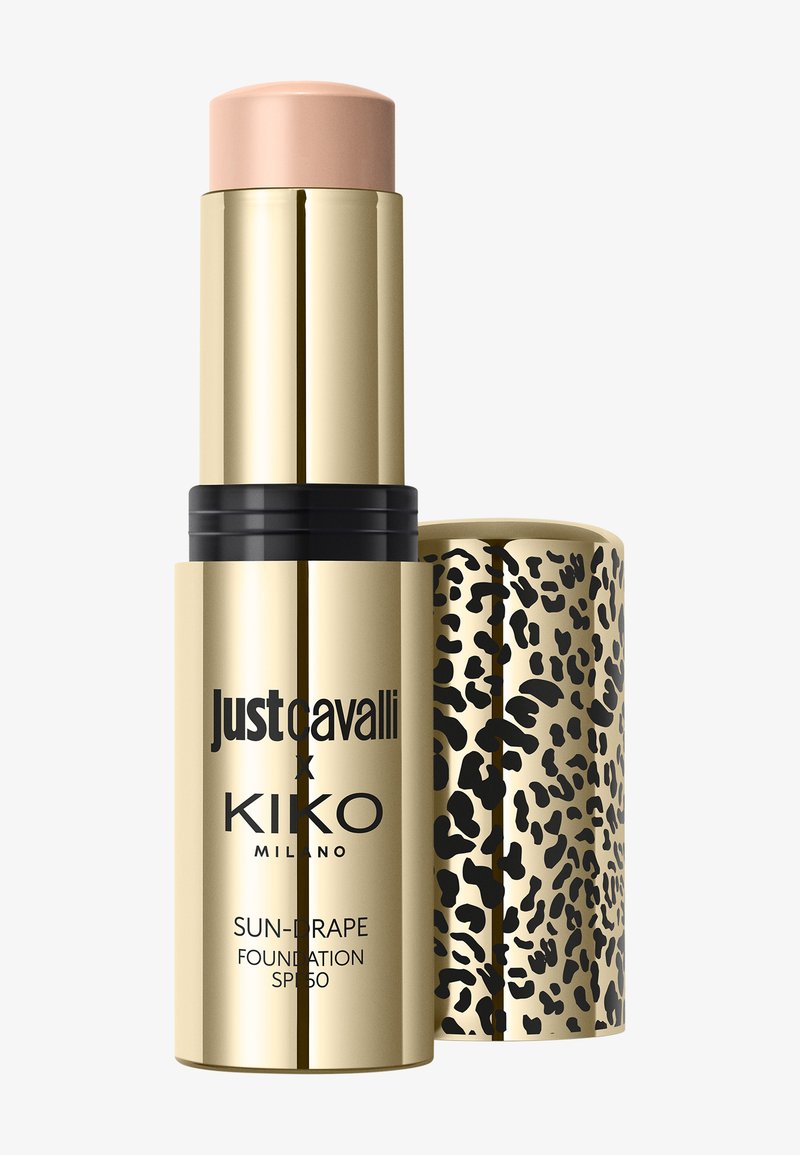 Gullfarget foundation-stick med beige sminke, svart tekst og leopardmønstret hette ved siden av, merket Just Cavalli x Kiko Milano SPF 50.