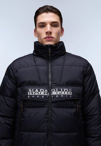 Schwarze Daunenjacke mit hohem Kragen, Reißverschluss und einer Brusttasche mit bedrucktem Logo. Sie verfügt über eine gesteppten Textur und genähtes Design.
