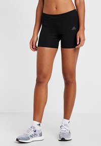 Pantalones cortos deportivos negros con un diseño ajustado, una cinturilla ancha y un pequeño logo gris en el lado izquierdo. Combinados con zapatillas grises y blancas.