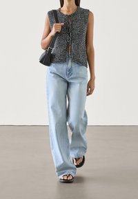 Czarnobiało nakrapiana bluzka na ramiączkach z detalem wiązania z przodu, w połączeniu z jasnoniebieskimi dżinsami o szerokich nogawkach i czarnymi sandałami.