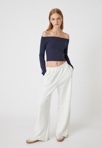 Schulterfreies, navy Blaues Langarm-Crop-Top, kombiniert mit weißen, weiten Hosen und beigen Sneakers, mit einem Kordelzugbund.