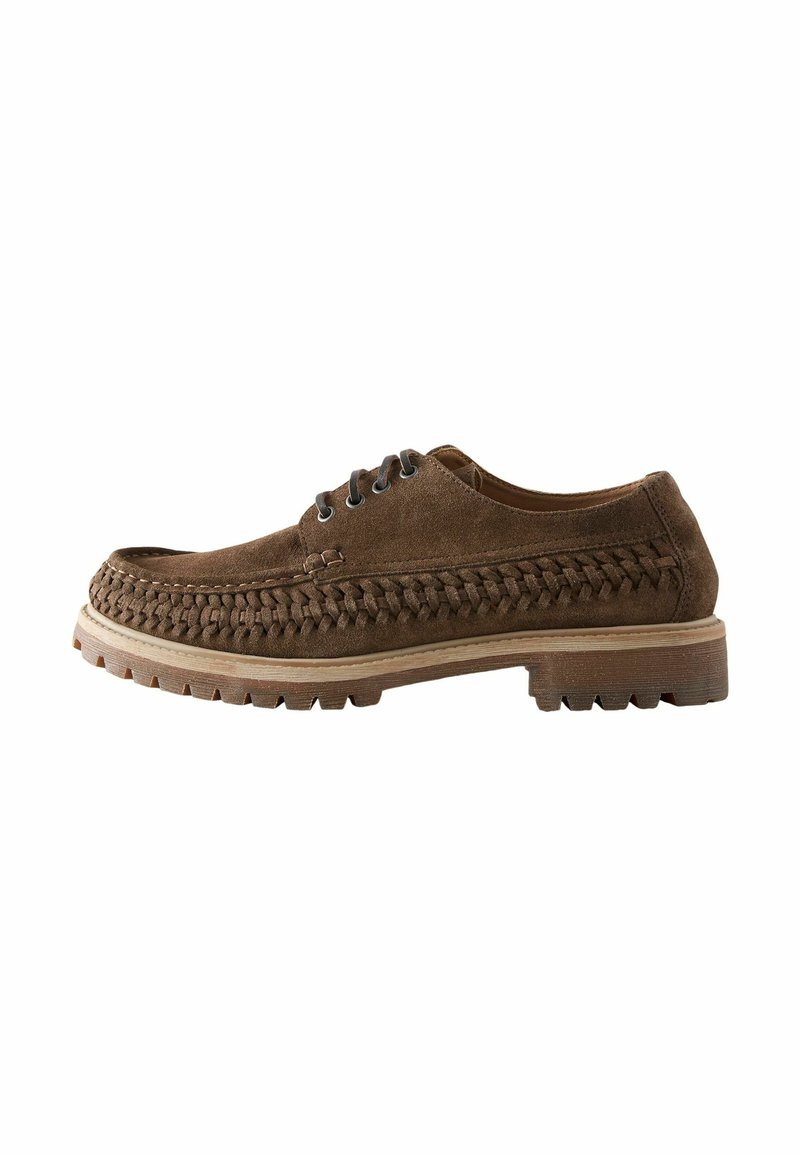 Chaussure en suède marron avec des détails tissés sur le bout et les côtés, bout arrondi, deux œillets pour les lacets, et une semelle en caoutchouc texturée.