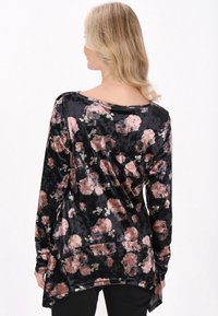 Langærmet bluse i sort velour med et blomstermønster, der har pink og hvide blomster. Flydende design med en længere ryg.