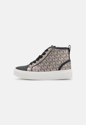 Basket montante avec bout et lacets noirs, côtés en tissu beige ornés d'initiales sombres répétées, et semelle blanche épaisse.