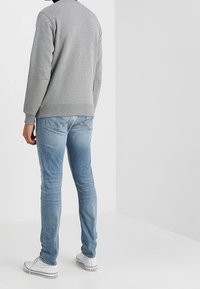 Grå sweatshirt med rund halsringning, parat med ljusblå jeans och vita sneakers. Synlig sömnad och detaljer på ärmarna av sweatshirten.