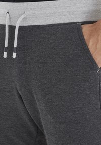 Dark grey jogger pants with a grey ribbed waistband, drawstring closure, and side pockets. Fabric is soft and textured.
