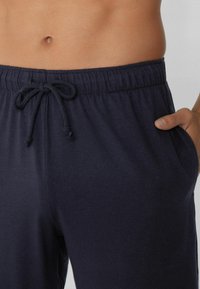 Námořnické bavlněné sportovní kalhoty s elastickým pasem, stahovací šňůrkou a bočními kapsami. Hladká textura s uvolněným střihem.