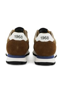 Un paio di sneakers marroni e beige con suole bianche e blu, viste da dietro, ciascuna etichettata "1968" sulla linguetta del tallone.