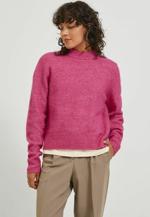 Maglione rosa lavorato a maglia con collo alto, maniche lunghe e orlo a costine. Texture morbida e vestibilità rilassata, abbinato a pantaloni beige chiaro.