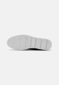 Baskets noires avec une semelle en caoutchouc blanc présentant un motif en zigzag. La semelle a une finition texturée et des marquages de taille sur la dessous.