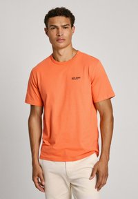 Oranžinė medvilninė marškinėliai trumpomis rankovėmis, apvaliu iškirpimu ir mažu juodu "PEPE JEANS" logotipu kairėje krūtinės pusėje.