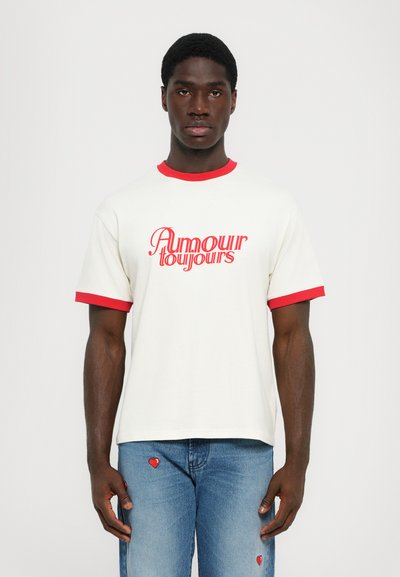 Cremefarvet kortærmet t-shirt med rød krave og ærmekanter, med teksten "Amour Toujours" skrevet i fed rød typografi.