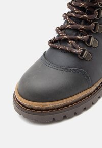 Botte en cuir bleu foncé avec un bout arrondi, lacets bruns, œillets en métal, accents cousus et semelle en caoutchouc texturé avec de profondesRAINURÉES.