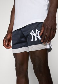 Mørkegrå mesh-shorts med hvite detaljer og en stor hvit logo på nederste venstre side. Har en løs passform og sideslitser.