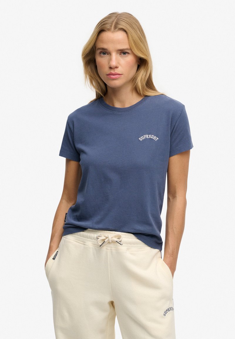 Marineblå bomulds-T-shirt med korte ærmer og rund hals, med hvid "Superdry" tekst på brystet, kombineret med lyse creme sweatpants.