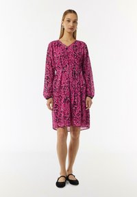 Rosa Blumenkleid mit langen Ärmeln und einem V-Ausschnitt, mit einer taillierten Taille und einem fließenden Rock. Schwarze Akzente an den Ärmeln.