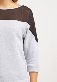 Grijze sweatshirt met een transparant zwart mesh paneel over de schouders, met een brede halslijn en driekwart mouwen. Zachte, gestructureerde stof.