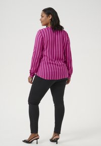 Magenta long-sleeve shirt with vertical white stripes, paired with black skinny jeans and sleek black heeled sandals. Smooth fabric and tailored fit.