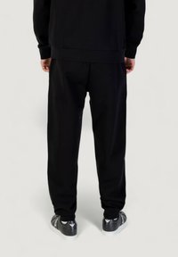 Schwarze Jogginghose aus weichem Stoff mit elastischem Bund, gerippten Bündchen und dezenten Logodetails. Kombiniert mit schwarzen Sneakers.