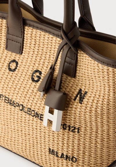 Πλέκτη τσάντα από άχυρο με καφέ δερμάτινες λεπτομέρειες, που διαθέτει μεταλλικό κλείδωμα και μαύρα γράμματα. Σχεδιασμός με ανοιχτό πάνω μέρος και διπλές χειρολαβές.
