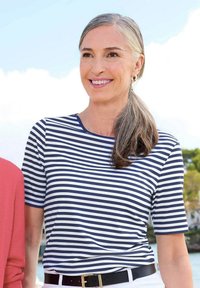 Navy und weiß gestreiftes Kurzarmhemd mit Rundhalsausschnitt, kombiniert mit einem schwarzen Gürtel, und über hellen Hosen getragen.