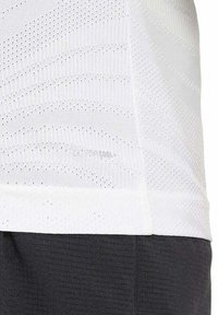 Camisa deportiva blanca de tejido que absorbe la humedad, con un patrón texturizado, perforaciones para la transpirabilidad y un diseño ajustado.