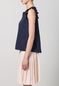 Navy blue sleeveless top with ruffled neckline, paired with a pleated blush skirt. Smooth texture with a fitted silhouette at the shoulders.