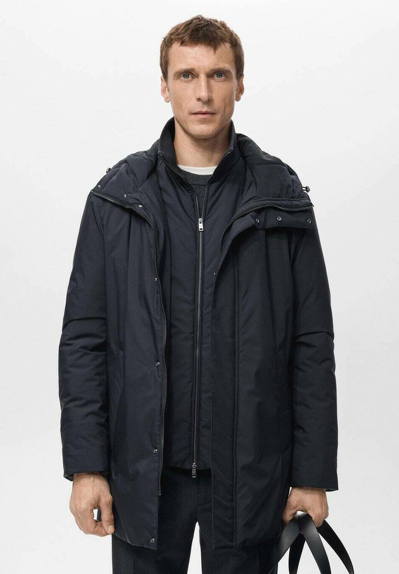 Cappotto imbottito nero con chiusura a zip, cappuccio rimovibile e due tasche laterali. Il tessuto sembra liscio con una finitura opaca.