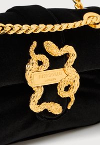 Juodas aksominis rankinukas su auksiniu gyvatės motyvu ir grandinine juosta. Metalinės detalės apima auksinę plokštelę su įspaudu "JUST CAVALLI MILANO".