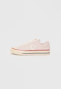 Sneaker in tela rosa con lacci crema e suola in gomma. Presenta un dettaglio a stella bianca, una striscia rossa vicino alla suola e un design classico a scarpa bassa.